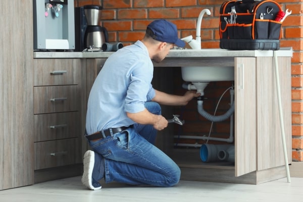 Plumber fixing a sink pipe with wrench.