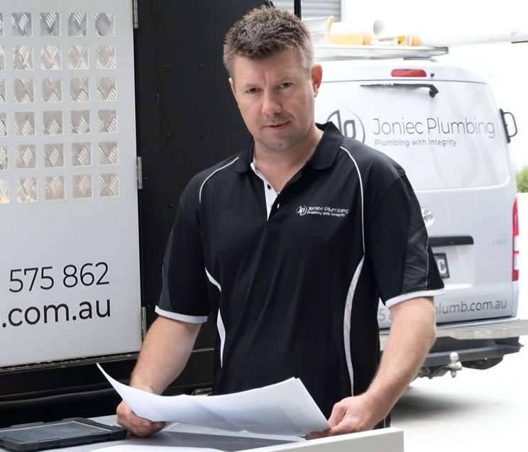 Blake the Plumber holding papers beside his company van.